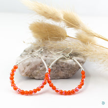 Load image into Gallery viewer, Handwrapped silver filled hoops with beautiful vibrant orange Czech glass 4mm beads on sterling silver ear wires. These earrings are lightweight, 5cm in drop length from the base of the earwires and 4cm in width. They come presented in a pretty gift pouch for safe keeping. Designed &amp; Handmade in Dingle
