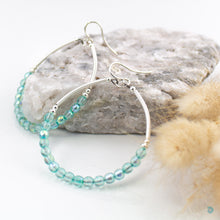 Load image into Gallery viewer, Handwrapped silver filled hoops with beautiful sea green Czech glass 4mm beads on sterling silver ear wires. These earrings are lightweight, 5cm in drop length from the base of the earwires and 4cm in width. They come presented in a pretty gift pouch for safe keeping. Designed &amp; Handmade in Dingle
