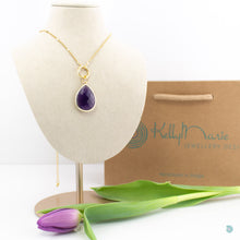 Load image into Gallery viewer, Large Amethyst teardrop pendant, sitting on a small chunky gold plated hoop, suspended on a gold plated stainless steel chain. This necklace is 20 inches in length with a 2inch extension chain. It comes presented in a pretty gift box for safe keeping or making it perfect for gift giving. Designed and made in Dingle
