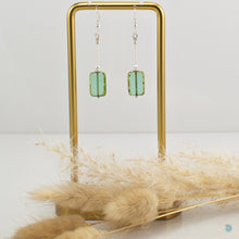 Load image into Gallery viewer, Hand wrapped silver filled drop earrings with a beautiful green Czech glass rectangular bead. These earrings sit on sterling silver ear wires and come with backs included. They are approximately 4cm in drop length from the base of the ear wires and are presented in a pretty gift pouch for safe keeping. Designed and handmade in Dingle

